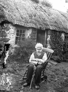 an old woman sitting in a chair next to a thatched house