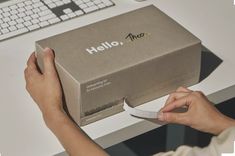 a person is opening a box on the desk with a keyboard and computer in the background