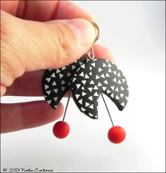 a pair of black and white earrings with red balls hanging from it's sides