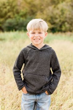 a young boy standing in tall grass with his hands on his hips and smiling at the camera