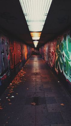 a long hallway with graffiti on the walls and ceiling above it is lit by a bright light