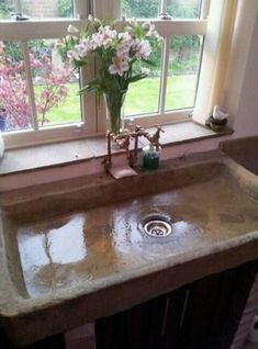 a bathroom sink sitting under a window next to a vase with flowers