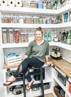 a woman sitting on top of a stool in a kitchen next to shelves filled with food