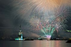 fireworks are lit up in the night sky over water and buildings with lights on them