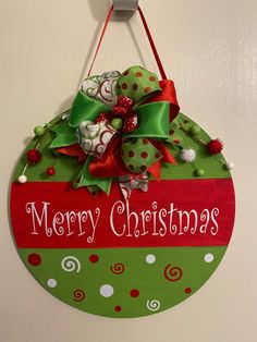 a merry christmas sign hanging on the wall with green and red ribbon around it's corner