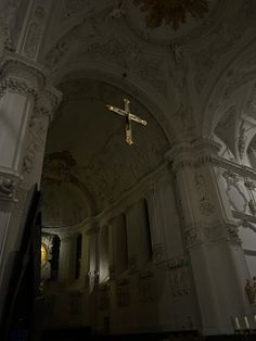 a cross hanging from the ceiling of a large building with white walls and ornate carvings