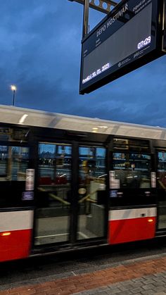 a red and white train traveling down tracks next to a street sign at dusk with dark clouds in the background