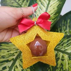 a hand holding a chocolate star ornament with a red bow on it's ribbon