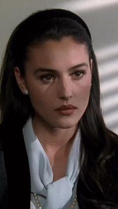 a woman with long dark hair wearing a white shirt and black blazer, looking at the camera