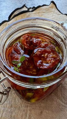 a glass jar filled with sliced tomatoes on top of a table