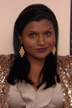 a woman with long black hair wearing large gold earrings on her head and sitting in a chair