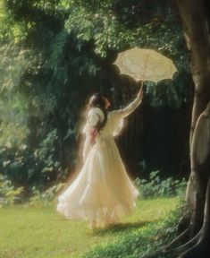 a woman in a white dress holding an umbrella next to a tree and grass field