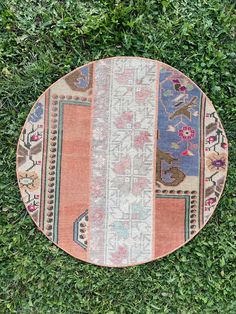 a round rug is laying on the ground with grass in the foreground and green plants behind it