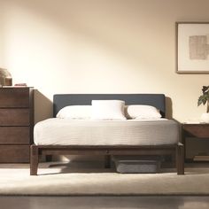 a bed with white sheets and pillows in a room next to a dresser, mirror and plant