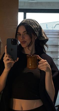 a woman taking a selfie with her cell phone and holding a cup in front of her