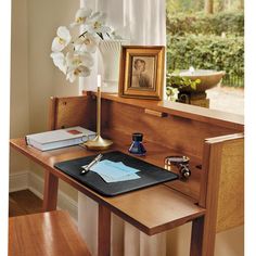 a wooden desk topped with a laptop computer next to a vase filled with white flowers