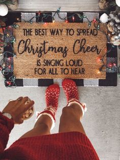 a woman standing in front of a christmas door mat that says the best way to spread christmas cheer is singing loud for all to hear