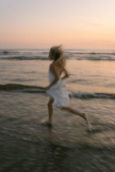 a woman running on the beach at sunset with her hair blowing in the wind,