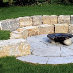 an outdoor fire pit surrounded by rocks and grass