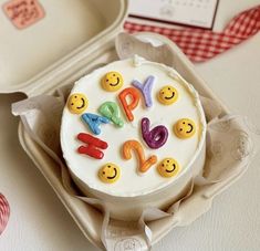 a birthday cake with smiley faces on it in a box next to a plate and spoon