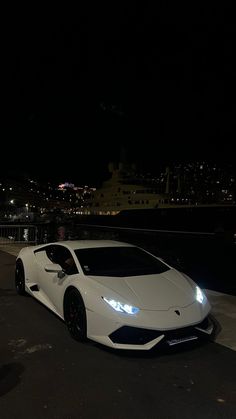 a white sports car parked in front of a cruise ship at night with the lights on