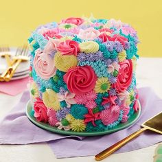 there is a colorful cake with flowers on the plate next to some forks and spoons