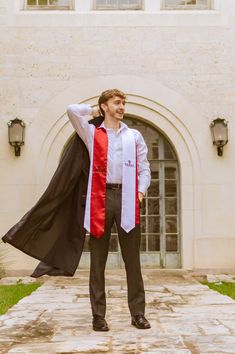 a man in a red and black robe is standing on a stone walkway with his hands behind his head