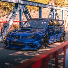 a blue car parked on the side of a road next to a red fence and some trees