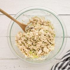 a glass bowl filled with tuna salad on top of a white wooden table next to a black and white striped napkin