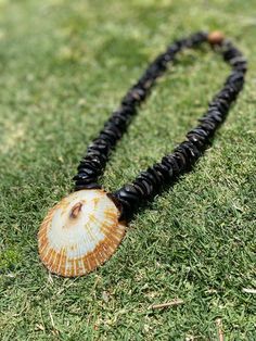 a necklace with a shell on it is laying in the grass and has beads attached to it