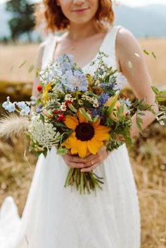 a woman in a white dress holding a bouquet of sunflowers and other flowers