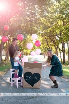 a family playing outside with balloons and a cardboard box that says it's a girl