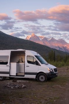 a white van parked in the middle of a field with mountains in the back ground