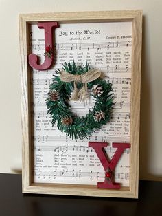 a wooden frame with a christmas wreath and letter j on top of sheet music paper