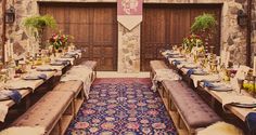 a long table set up with place settings and flowers in front of a stone wall