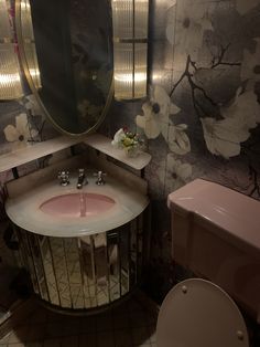 a pink sink and toilet in a small room with floral wallpaper on the walls