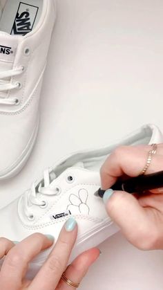 a woman is drawing on a pair of white tennis shoes with black marker and pen