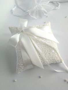 a white wedding ring pillow with ribbon and pearls on the side, sitting on a table