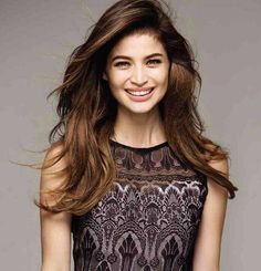 a woman with long hair smiling and wearing a black lace top, posing for the camera