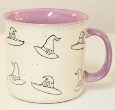 a purple and white coffee mug with witches on it's side, sitting on a table