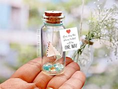 a person holding a tiny ship in a bottle filled with confetti and seaweed