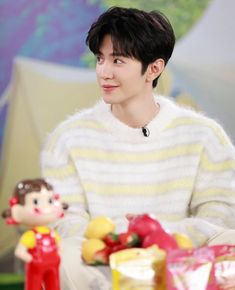 the young man is sitting down with his doll in front of him and wearing a striped sweater