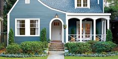 a blue house with white trim and two windows on the front door is surrounded by greenery