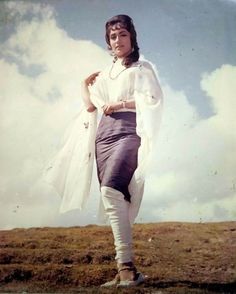 a woman standing on top of a grass covered field next to a sky filled with clouds