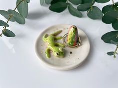 a frog figurine sitting on top of a white plate next to green leaves