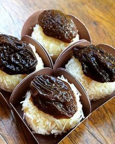 four pastries with chocolate sauce on top of rice in a cardboard box sitting on a wooden table