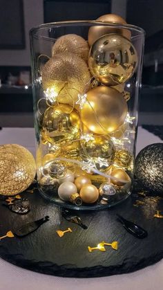 a glass vase filled with ornaments on top of a black table covered in gold and silver balls