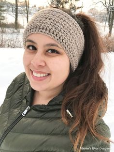 a young woman wearing a knitted beanie smiles at the camera while standing in the snow