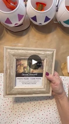 a person holding up a framed photo in front of some cups and bowls on a table