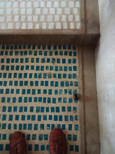 someone's feet are standing in front of a tiled floor